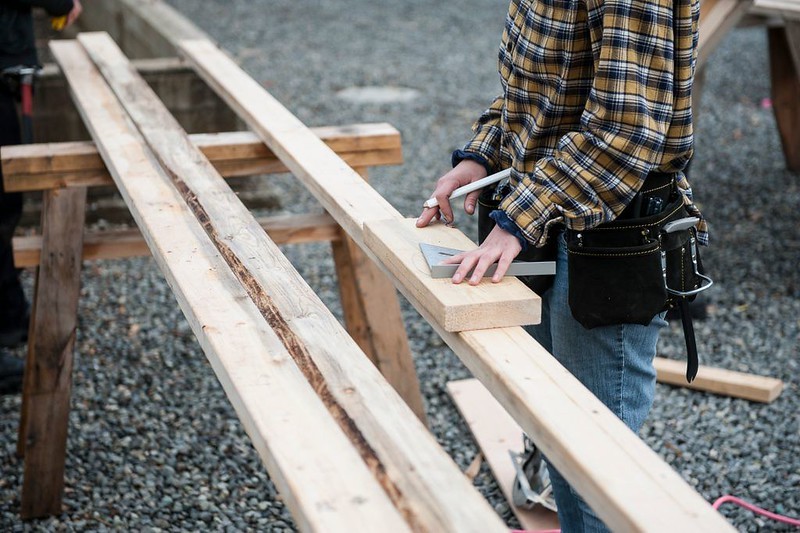 A worker measures a piece of lumber.